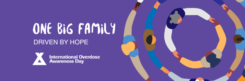 Purple banner that says one big family driven by hope. Depicts a bird's eye view of people standing in concentric circles holding hands.